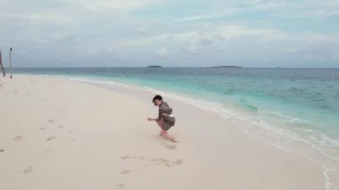Sahilde dans eden neşeli bir kadının havadan çekilmiş görüntüsü, Maldivler 'deki Hint okyanusunun ufuk çizgisi ve turkuaz dalgaları. Hayallere yolculuk kavramı