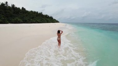 Sahilde koşan genç bir kadının hava görüntüsü, turkuaz dalgalar ve Maldivler 'de tropikal ormanlı Hint okyanusu. Turizm ve mutluluk kavramı