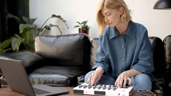 Woman playing on midi controller in living room with couch, producer of music with laptop on table. Music producer at home studio with professional equipment.