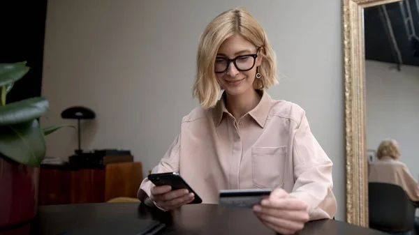 Blondine Vrouw Bril Geconcentreerde Look Telefoon Creditcard Handen Online Winkelen Rechtenvrije Stockfoto's