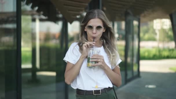 カジュアルな服とサングラスで魅力的な若い女性は 笑顔と冷たい飲み物を飲む夏の公園に立っています ストリート ファッション ライフ スタイル コンセプト — ストック動画