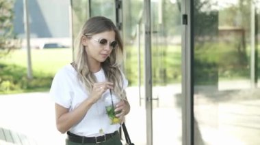 Çekici genç kadın güneş gözlüğü ve rahat kıyafetler yaz Park'ta yürüyordunuz ve soğuk bir mohito içiyor. Sokak moda yaşam tarzı kavramı. Yavaş hareket orta atış izleme