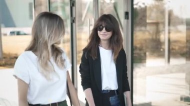 İki çekici genç blogcular, Sarışın, kahverengi saçlı, içinde güneş gözlüğü moda ve rahat kıyafetler birlikte sokak moda trendleri yaz Park tartışırken yürüyor. Yavaş hareket orta atış izleme