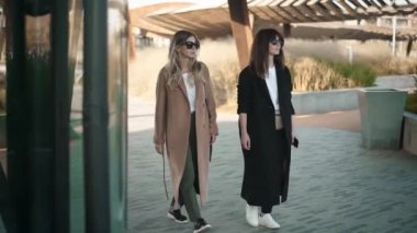 Sarışın ve esmer genç kadınlar şık giysiler ve güneş gözlüğü sonbahar sokak yürüyüş mesafesindedir. Sosyal medya ve moda yaşam tarzı kavramı. Yavaş hareket orta atış izleme