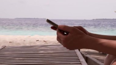 Genç bir kadın sahilde akıllı telefon kullanıyor. Yaşam tarzı. Deniz kıyısında boş zaman aktiviteleri. Yüksek kalite 4k görüntü