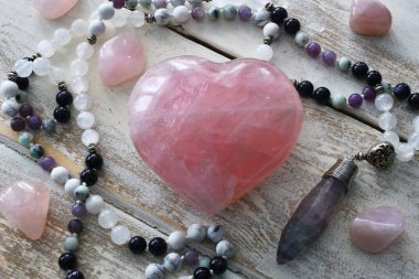 Üzerinde meditasyon mala kolyesi olan gül kuvars kristal bir kalbin üst görüntüsü.. 