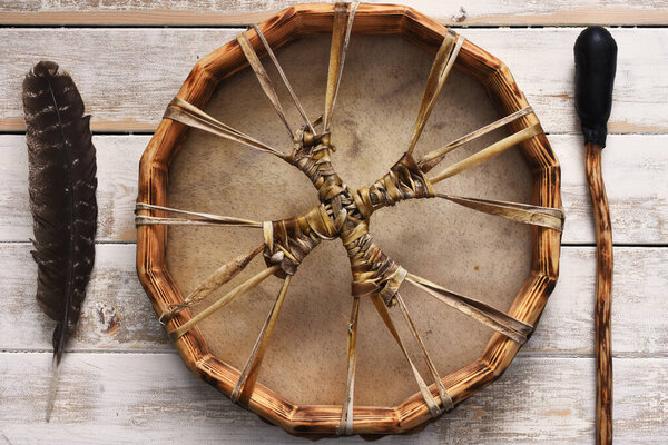A top view image of the intricate lacing of a hand made leather meditation drum with sacred feather on a white washed table. 