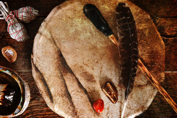 A top view image of a handmade leather meditation drum with sage smudge sticks and healing crystals. 