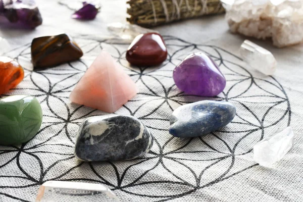 A close up image of chakra healing crystals arranged on sacred geometry grid cloth with rose quartz pyramid.