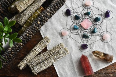 A top view image of a healing crystal grid using a sacred geometry grid cloth and white sage smudge sticks. clipart