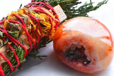 A close up image of a cedar smudge stick wrapped in bright red thread with a carnelian geode.  clipart