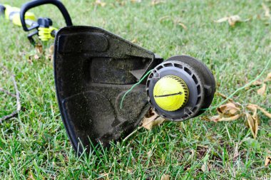 A close up image of the dirty underside of an electric weed whacker used in lawn maintenance. 
