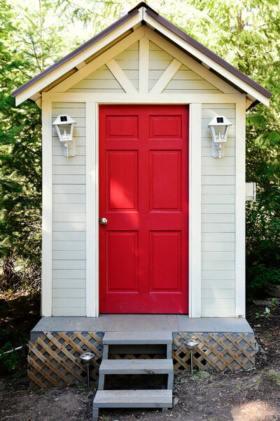 An image of an outdoor composting toilet with a bright red door and solar powered lights. 