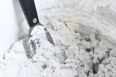 A close up image of white drywall plaster in a white pail with a drywall trowel. 