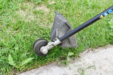 An image of a black and yellow weed whacker trimming the grass alongside a sidewalk. 
