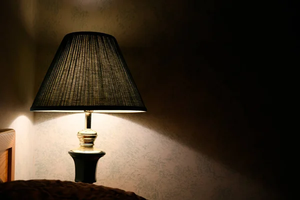 An image of a old lamp with green lamp shade in an old run down motel room.