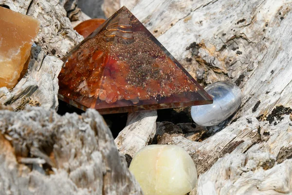 A close up image of several healing crystals with orgonite pyramid resting on a rough piece of driftwood.
