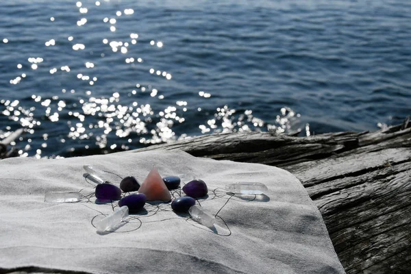 An image of a crystal grid set up on a large piece of driftwood with the ocean in the background.