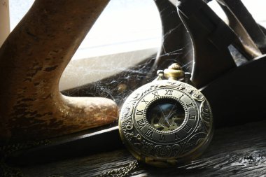 Ahşap bir çıkıntıda dinlenen ve örümcek ağlarıyla kaplı eski bir cep saatinin görüntüsü..