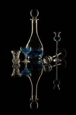 Zarif içki bardakları ve siyah arka planda mavi likör şişesi.