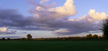 Kümülüs bulutları ve güneş panoramik manzaralı yeşil çimen tarlası