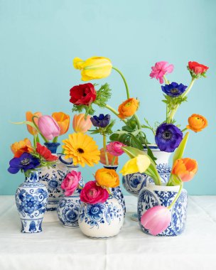 A Lush natural light stillife with old Dutch Delft blue lidded vase with multicolored flowers on white linen against a blue background clipart