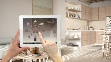 Dijital tablette akıllı uzaktan kumanda sistemi. Uygulama simgeleri olan aygıt. Rahat sürdürülebilir mutfak, oturma odası, kanepe çaydanlık ve çay fincanlı masalar, mimari iç tasarım.