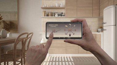 Dijital akıllı telefon tabletindeki uzaktan kumanda sistemi. Uygulama simgeleri olan aygıt. Ahşap mutfak, yemek masası, arka planda sandalyeler, mimari tasarım.