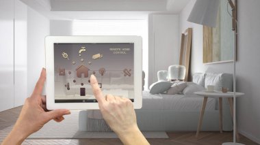 Dijital tablette akıllı uzaktan kumanda sistemi. Uygulama simgeleri olan aygıt. Minimalist, parlak yatak odası, arka planda ana yatak, mimari iç tasarım.