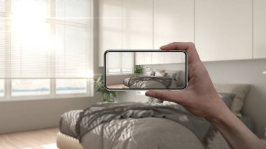 El ele tutuşan akıllı telefon, AR uygulaması, gerçek evde mobilya ve iç tasarım ürünleri simülasyonu, mimar tasarım konsepti, bulanık arka plan, yatak ve dekorlu modern yatak odası