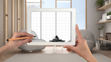 El ele tutuşup tablete resim çizerek modern oturma odasını Japon stili CAD çizimleriyle gösteriyor. Arka planda gerçekten bitmiş iç mimari tasarım sunumu