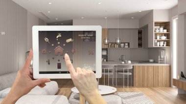 Dijital tablette akıllı uzaktan kumanda sistemi. Uygulama simgeleri olan aygıt. Minimalist, yemek masası olan parlak bir mutfak, arka planda sandalyeler, mimari iç tasarım.