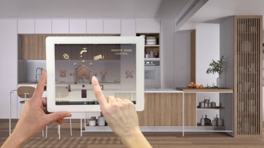 Dijital tablette akıllı uzaktan kumanda sistemi. Uygulama simgeleri olan aygıt. Minimalist, arka planda ada ve dolapları olan, mimari iç mimari tasarımı olan parlak bir mutfak.