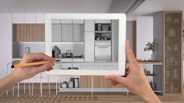 Tablet üzerinde el ele tutuşup çizim yaparken ada ve tabure ile modern mutfağı gösteriyor. Arka planda gerçekten bitmiş iç mimari tasarım sunumu