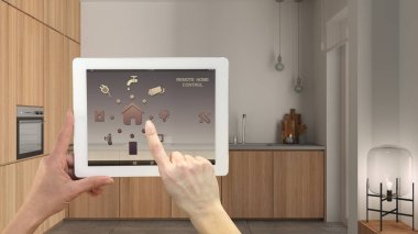 Dijital tablette akıllı uzaktan kumanda sistemi. Uygulama simgeleri olan aygıt. Arka planda dolapları ve aletleri olan rahat ahşap mutfak, mimari iç tasarım.