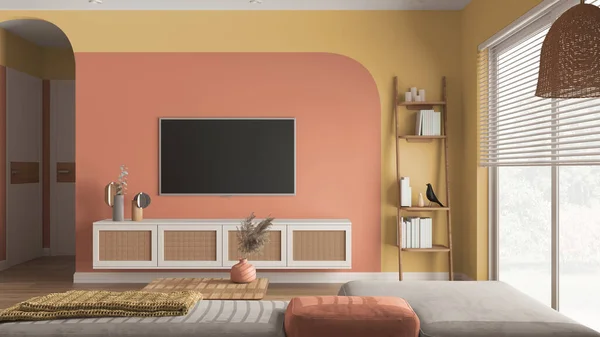 Modern wooden living room in orange tones, velvet sofa with side table, rattan commode with television, ladder shelves with books and decors. Big window with blinds. Interior design