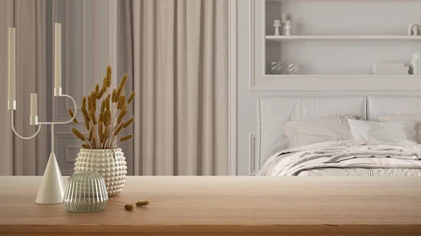 Wooden table, desk or shelf close up with ceramic and glass vases with dry plants, straws over classic bedroom with bed, molded walls, arched doors, curtains, interior design concept