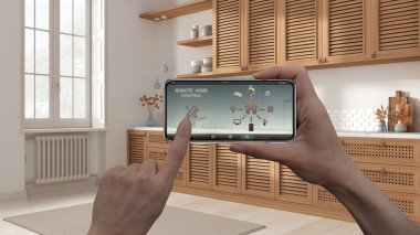 Dijital akıllı telefon tabletindeki uzaktan kumanda sistemi. Uygulama simgeleri olan aygıt. Ülke içi ahşap mutfak, arka planda panjurlu dolaplar, mimari tasarım.