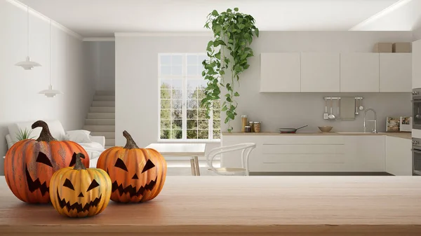 Halloween carved pumpkins on wooden table. Autumn decoration over interior design scene. Modern country kitchen with dining table and sofa