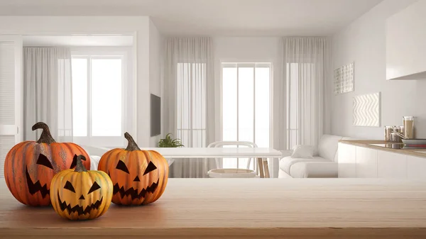 Halloween carved pumpkins on wooden table. Autumn decoration over interior design scene. White modern kitchen with dining table and chairs