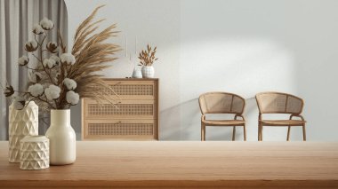Wooden table, desk or shelf close up with ceramic vases with cotton flowers over wooden living room with rattan furniture, boho style interior design concept