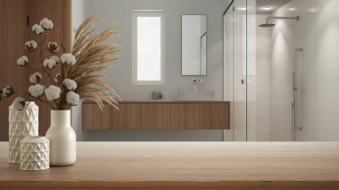 Ahşap masa, masa ya da raf minimalist banyo, lavabo ve duş, boho tarzı iç dizayn konsepti üzerine pamuk çiçekli seramik vazolarla kapatın.