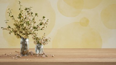 Ahşap masa, masa ya da rafı kapat. Cam vazoda kiraz dalları çiçek açar. Alçıyla boyanmış duvar sarı tonlarda kopya alanı, şablon, model, bahar konsepti