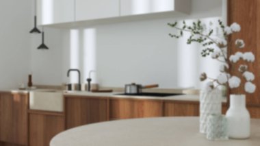 Blurred background, japandi trendy wooden kitchen and dining room. Close up on table with cotton flowers, cabinets and marble top. Minimalist interior design