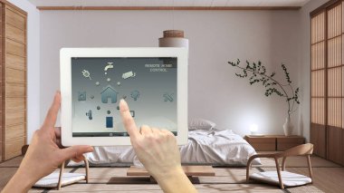 Dijital tablette akıllı uzaktan kumanda sistemi. Uygulama simgeleri olan aygıt. Arka planda minimalist modern japandi yatak odası, mimari iç tasarım.