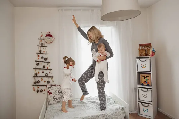 Mutter und Kinder springen morgens im Schlafanzug auf das Bett — Stockfoto