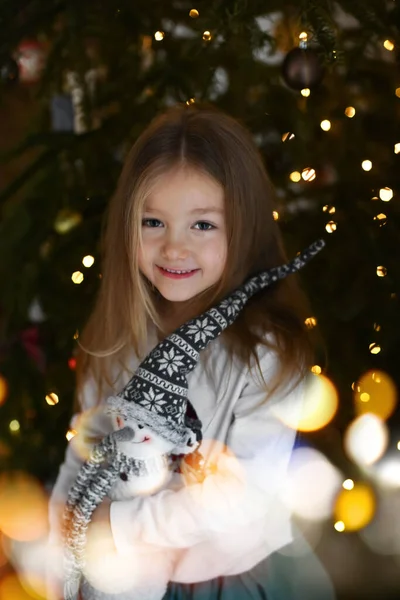 クリスマスツリーの近くで雪だるまのおもちゃを抱きかかえている女の子 — ストック写真