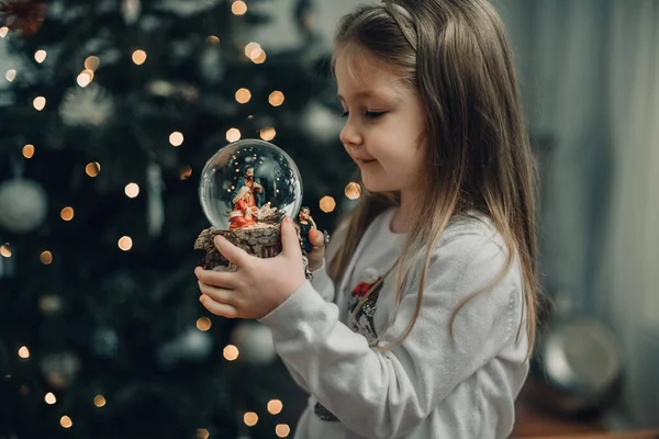 クリスマスツリー上のガラスボールにイエス キリストのネイティブのシーンとガラスボールを見て女の子 — ストック写真