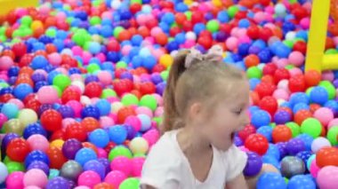 Plastik toplarla ortada oynayan kuru bir yüzme havuzunda bir kız..