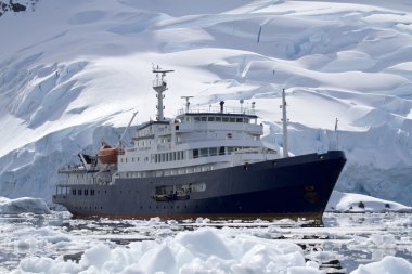 big blue tourist ship in Antarctic waters against the backdrop o clipart